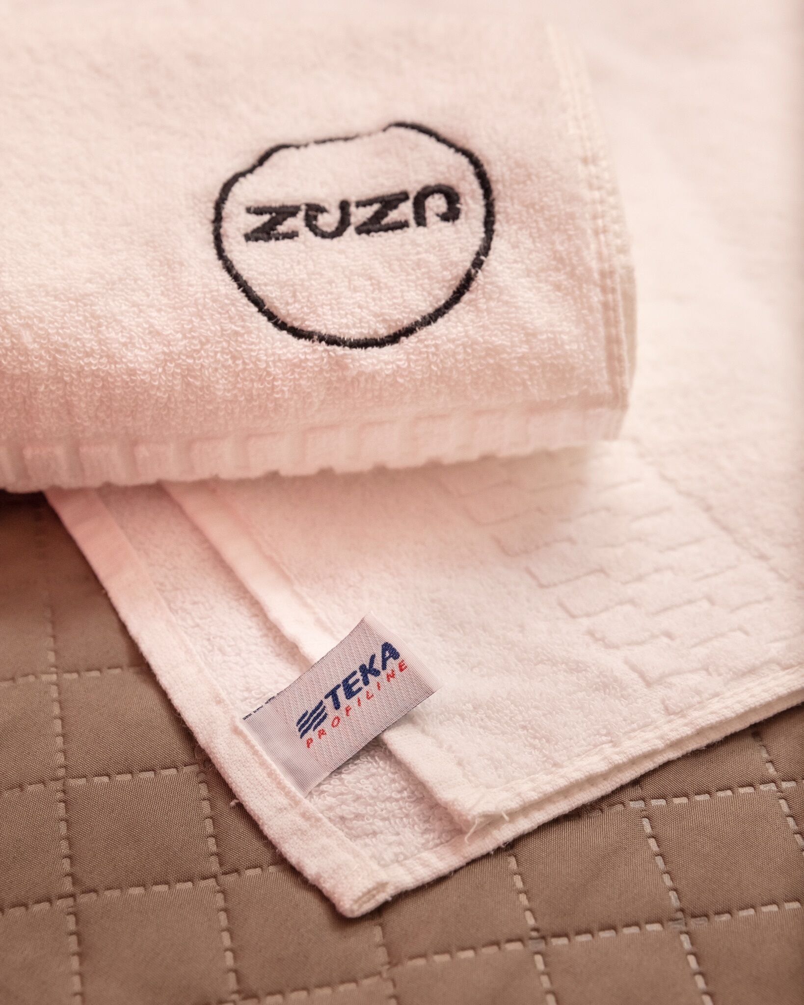 A folded beige quilted towel with a visible brand tag.