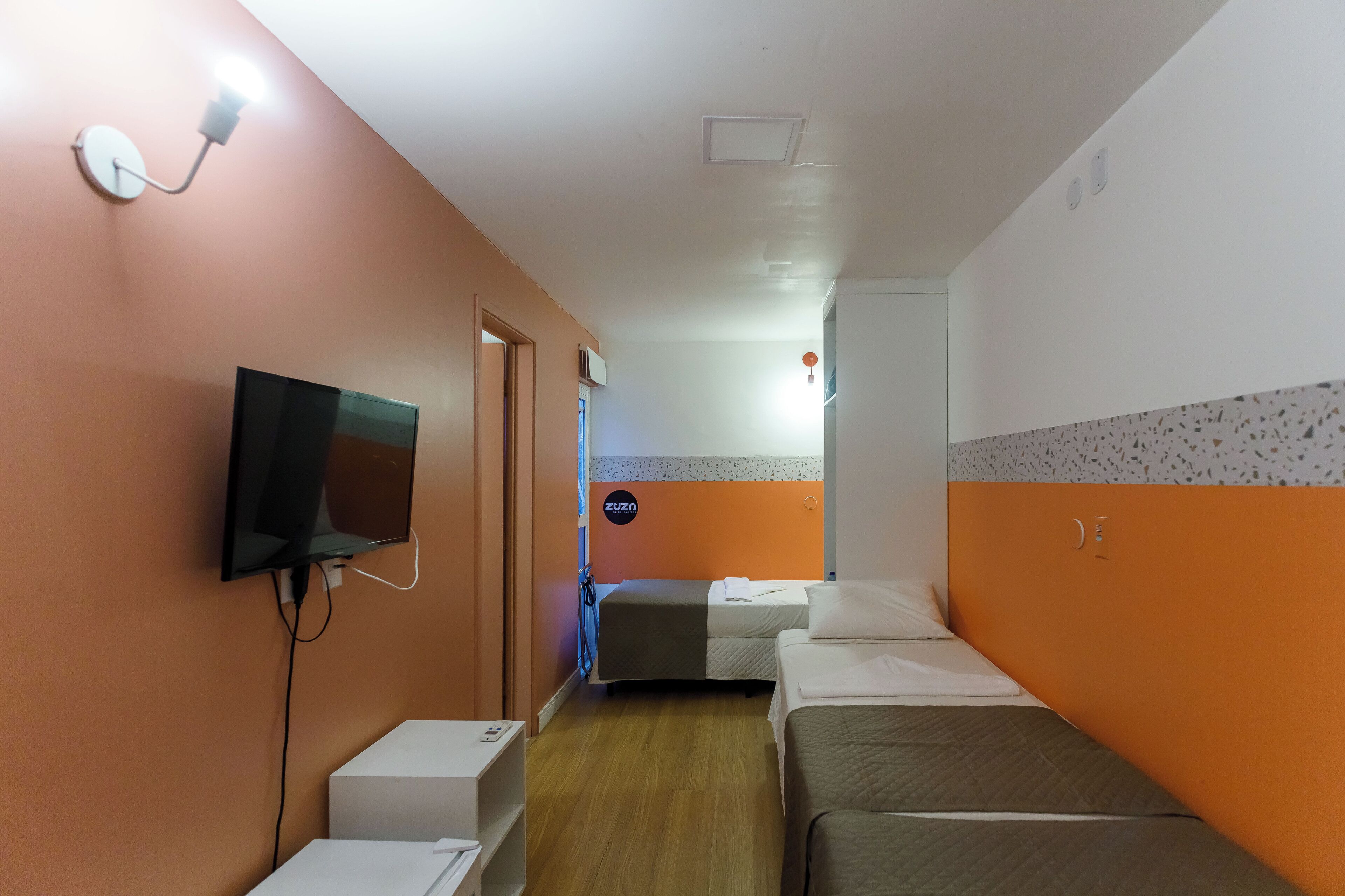 Habitación de hotel con una televisión montada en la pared, una cama, una mesita de noche y un escritorio pequeño.