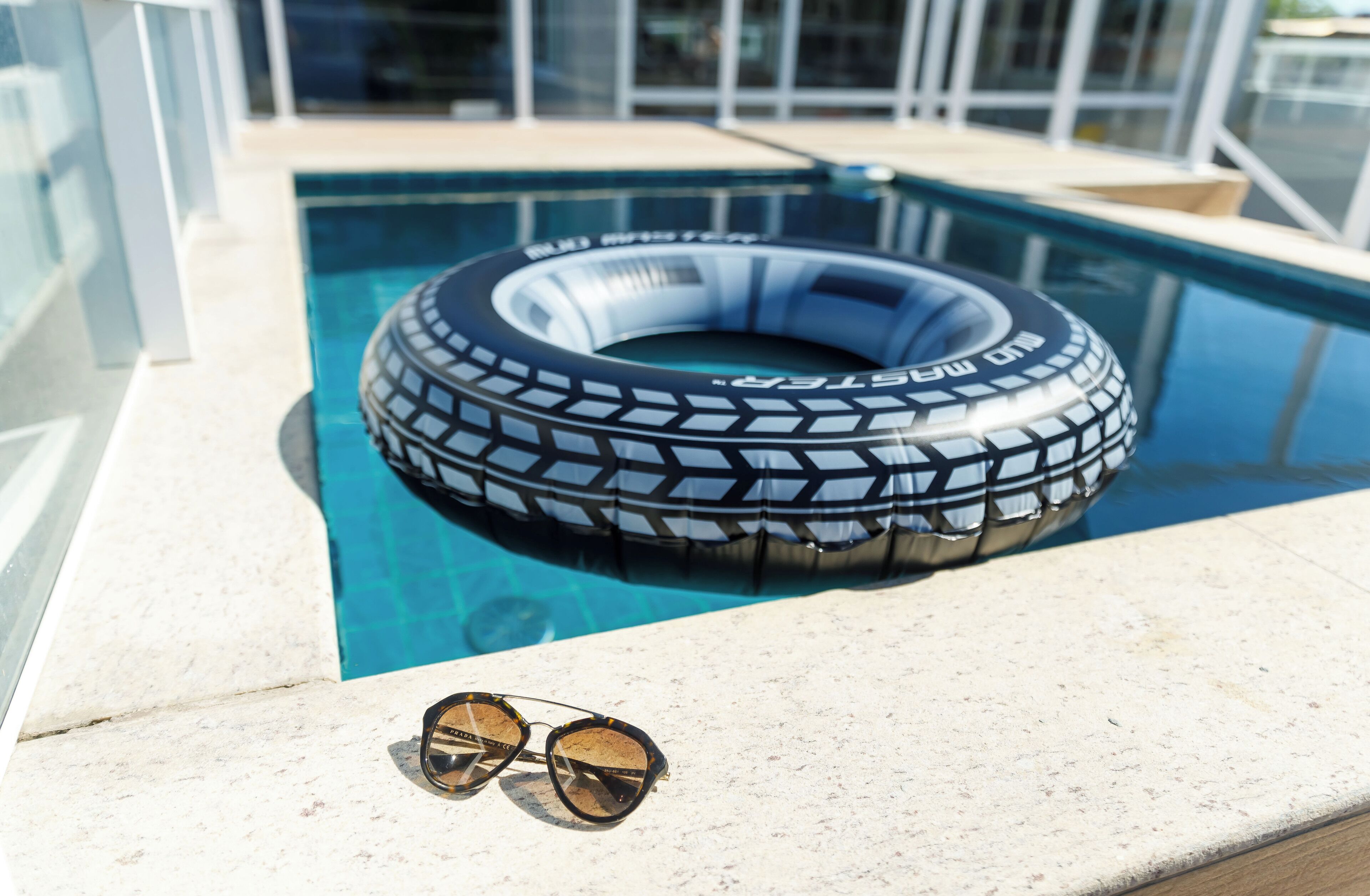 A pool with a tire float and sunglasses on the edge.