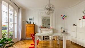 A dining area with a glass table, clear chairs, a wooden cabinet, and a chandelier.
