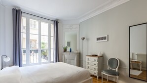 A bedroom with a large bed, a dresser, a chair, a mirror, and a window with curtains.
