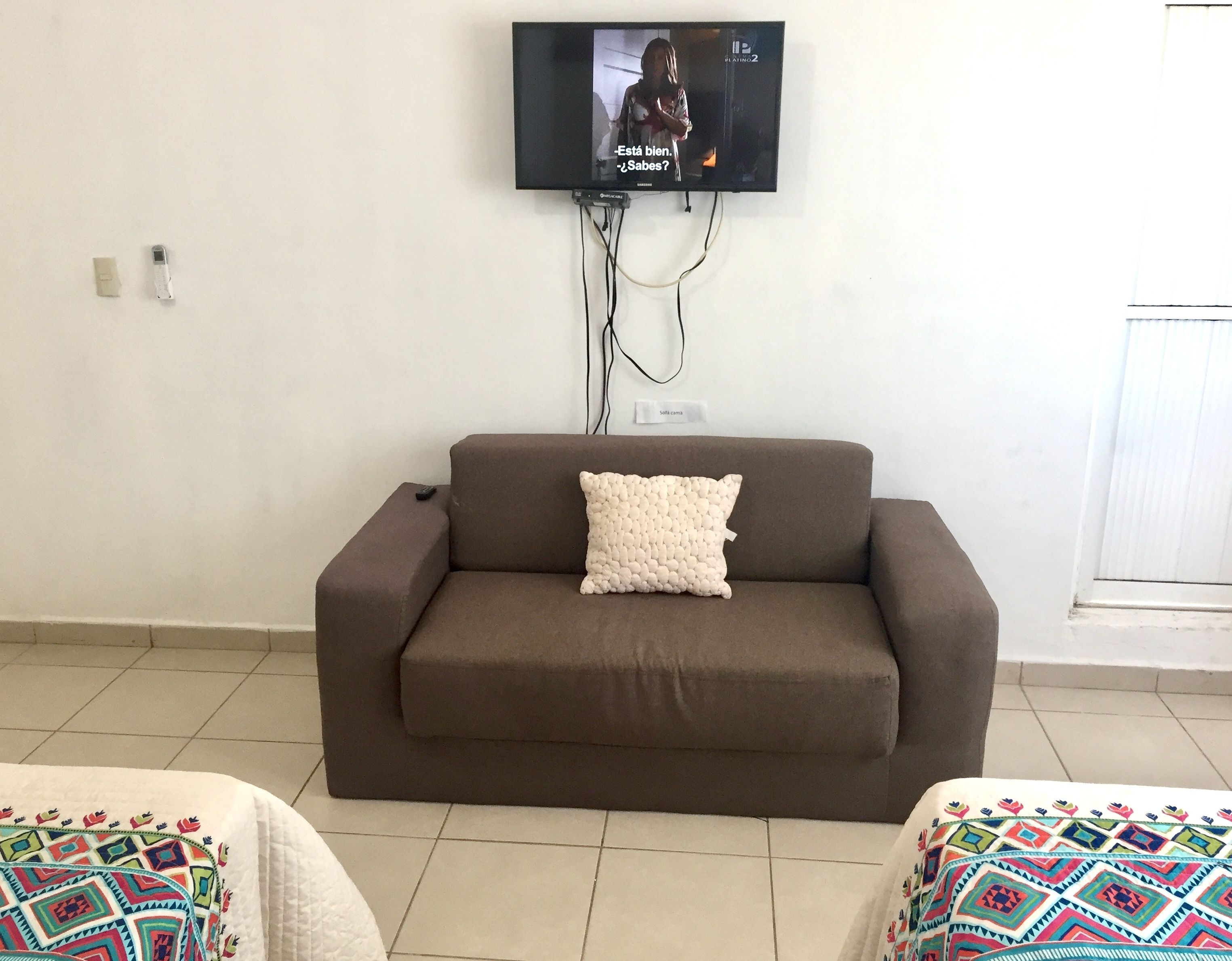 Una sala de estar con un sofá marrón, un cojín blanco texturizado y un televisor montado en la pared.