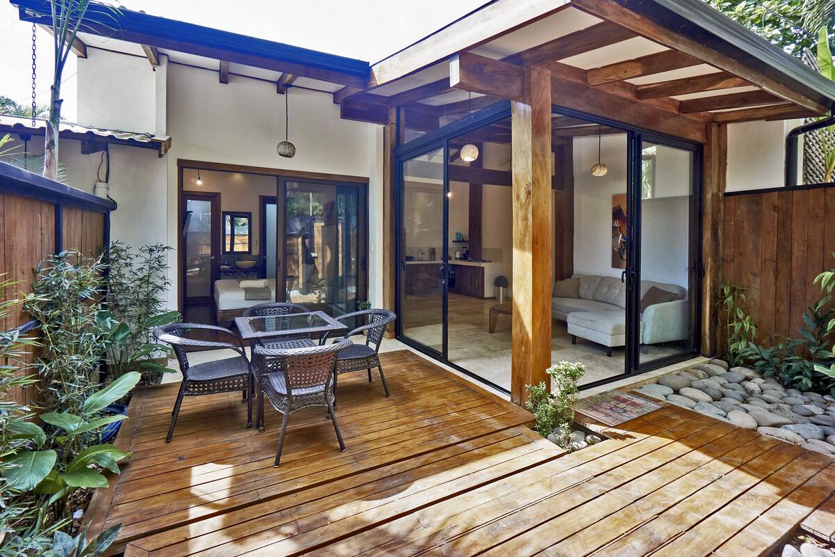 A wooden deck with a table and chairs, surrounded by potted plants.