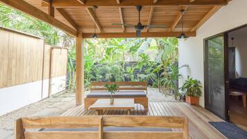 A wooden deck with benches and a table, surrounded by lush greenery.