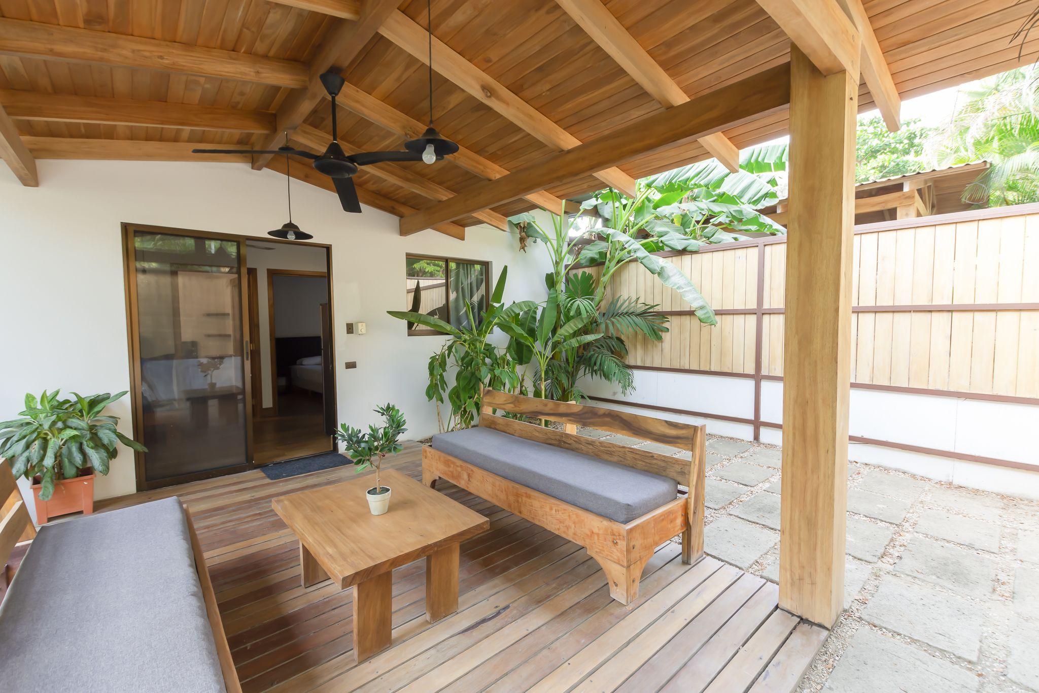 A wooden deck with a bench, table, and potted plants.