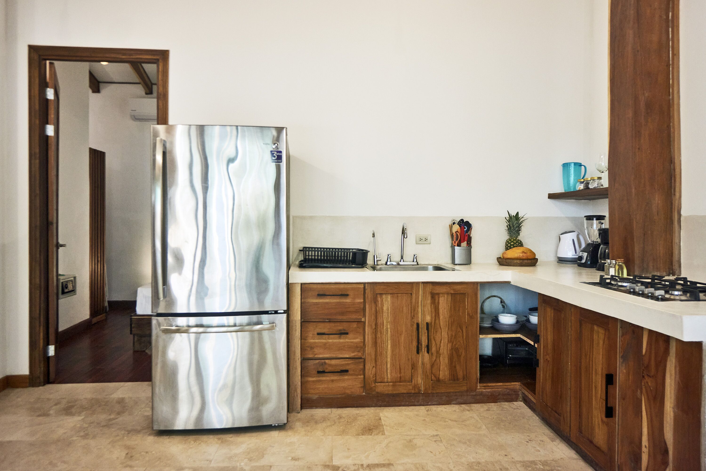 Une cuisine moderne dotée d’un réfrigérateur en acier inoxydable, de meubles en bois, d’un plan de travail blanc et d’un four encastré.
