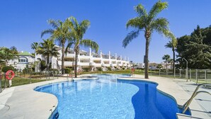 Ein Pool mit geschwungener Kante, umgeben von Palmen und einem Gebäude mit mehreren Balkonen im Hintergrund.