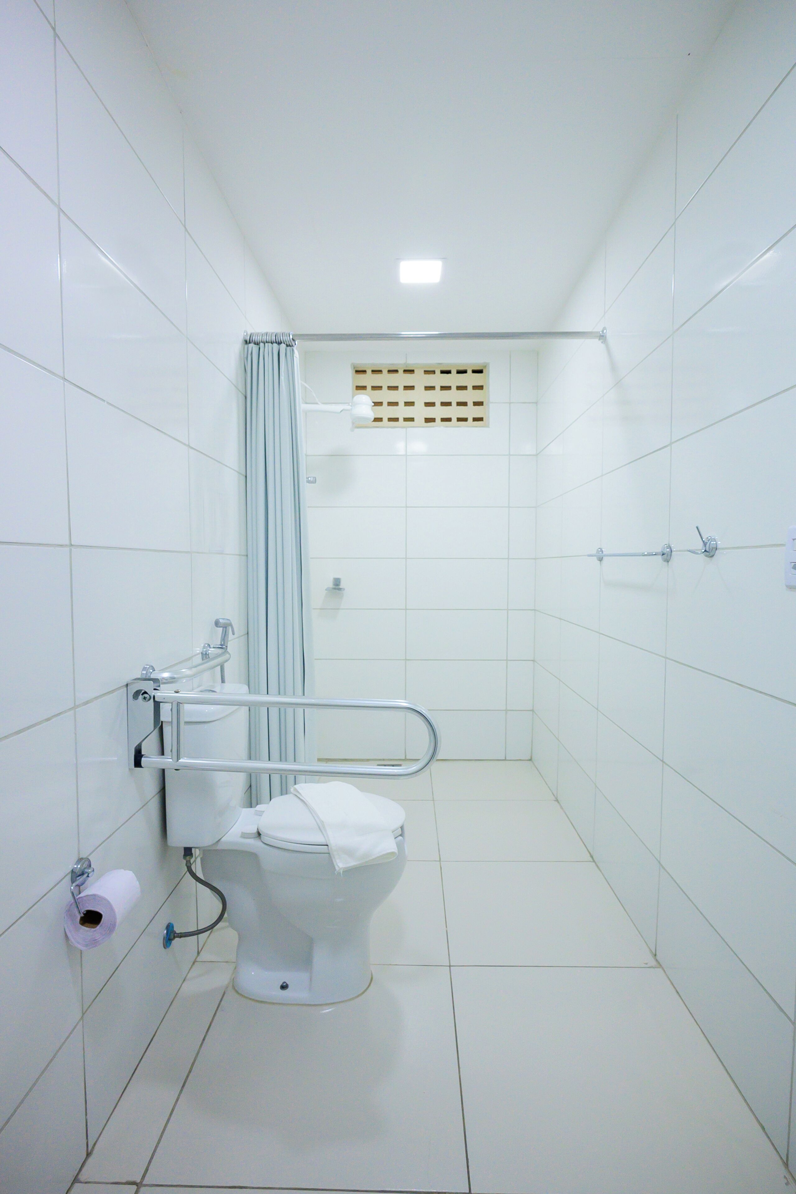 Un baño pequeño y blanco con inodoro, barandilla y cortina de ducha.