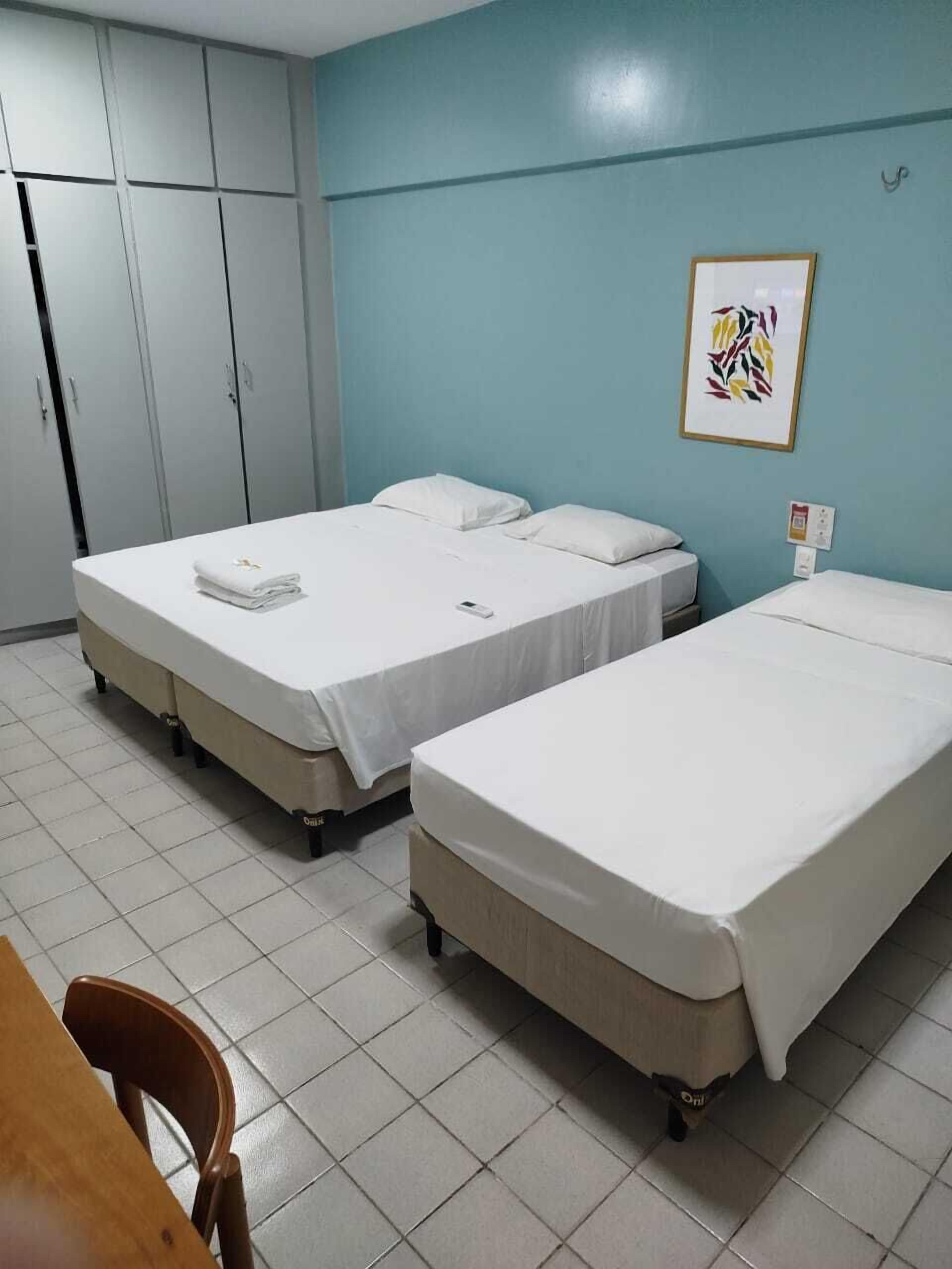 Ein Hotelzimmer mit zwei Einzelbetten, einem Schrank, einem Tisch und einem gerahmten Bild an der Wand.