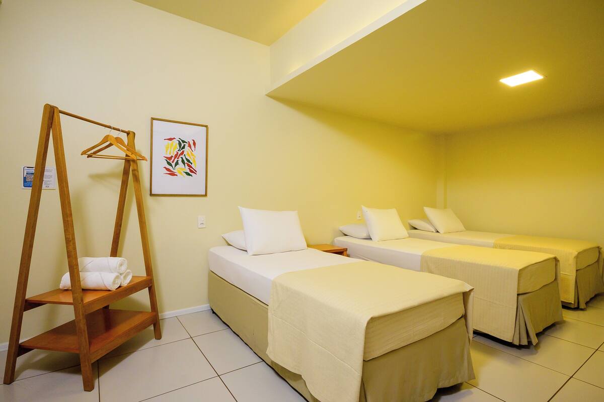 A hotel room with two single beds, a wooden shelf with towels, and a framed picture on the wall.