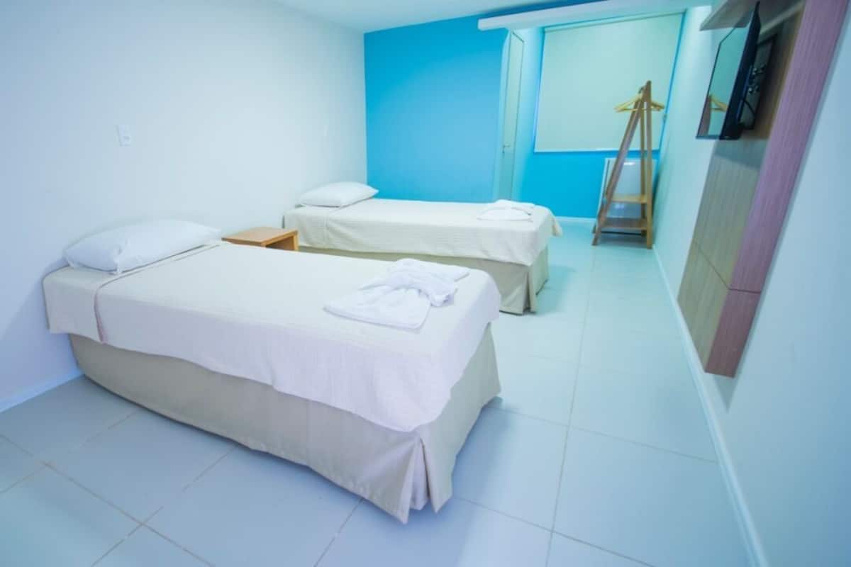 A hotel room with two beds, a wardrobe, and a mirror.
