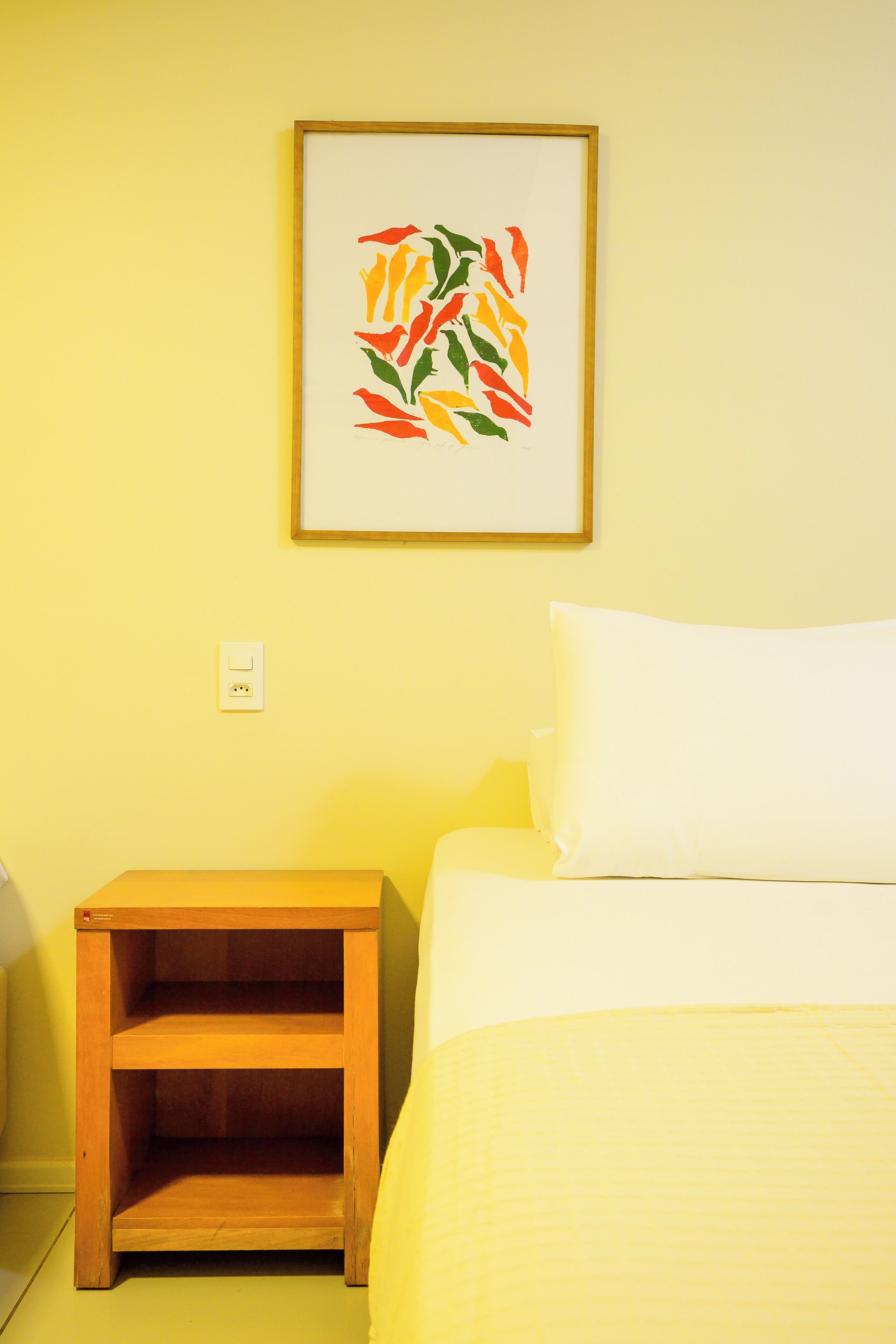 Una habitación con una cama, una mesita de noche y una obra de arte enmarcada en la pared.
