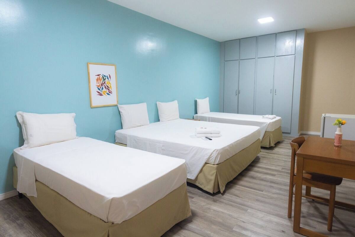 A hotel room with three single beds, a wooden table, and a cabinet.