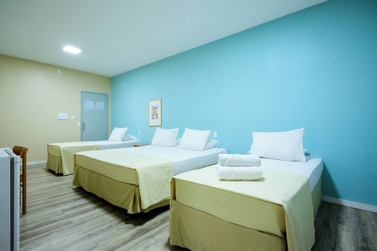 A hotel room with three beds, a wooden floor, and a light blue wall.