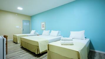 A hotel room with three beds, a wooden floor, and a light blue wall.