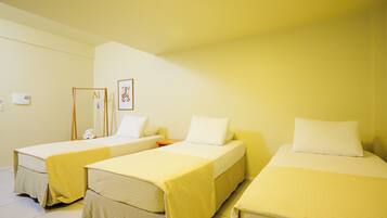 Ein Hotelzimmer mit drei Einzelbetten, jedes mit einer gelben Tagesdecke und weißen Kissen. Es gibt einen kleinen Nachttisch mit einer Lampe und einen an der Wand montierten Heizkörper.