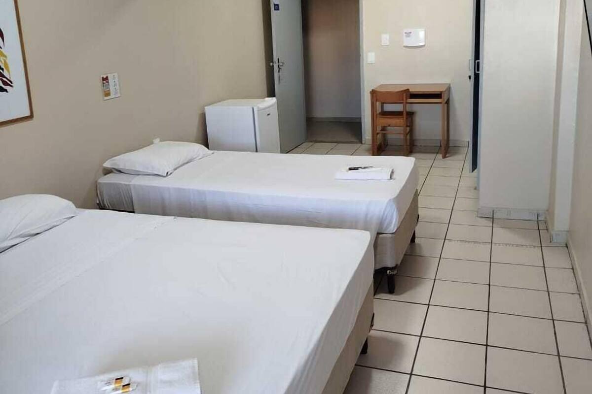 A hotel room with two beds, a small desk, and a door leading to a hallway.