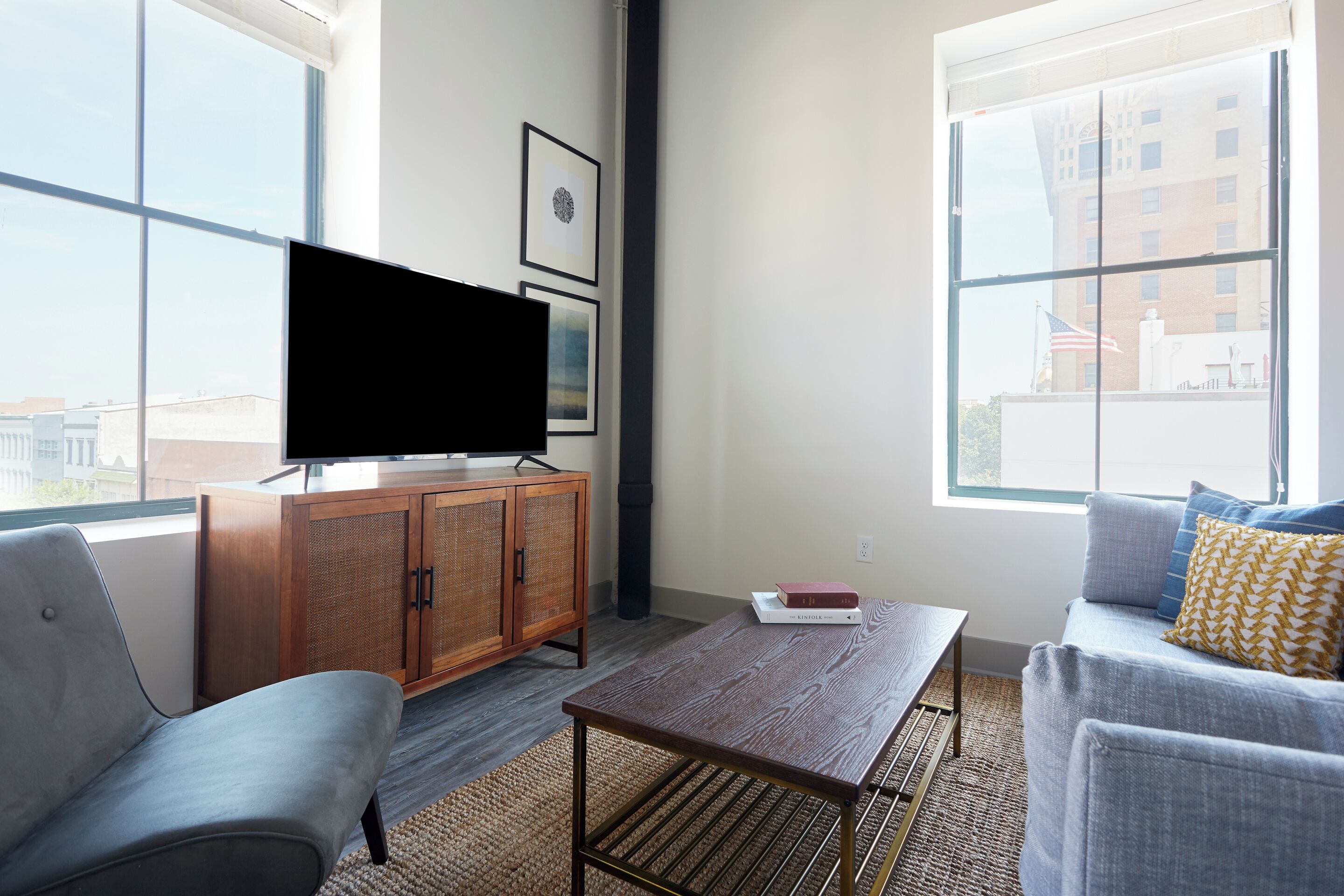 Een moderne woonkamer met een groot raam, een flatscreen televisie, een houten kast, een bank en een salontafel.