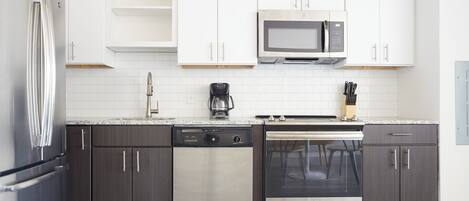 A modern kitchen with stainless steel appliances, white cabinetry, and a tiled backsplash.