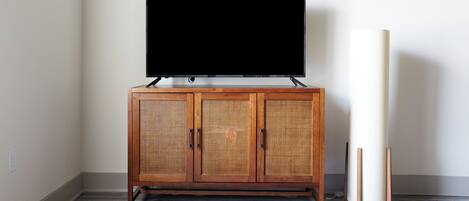 Un mueble de madera con un televisor encima, un objeto cilíndrico blanco a su lado y un suelo gris.