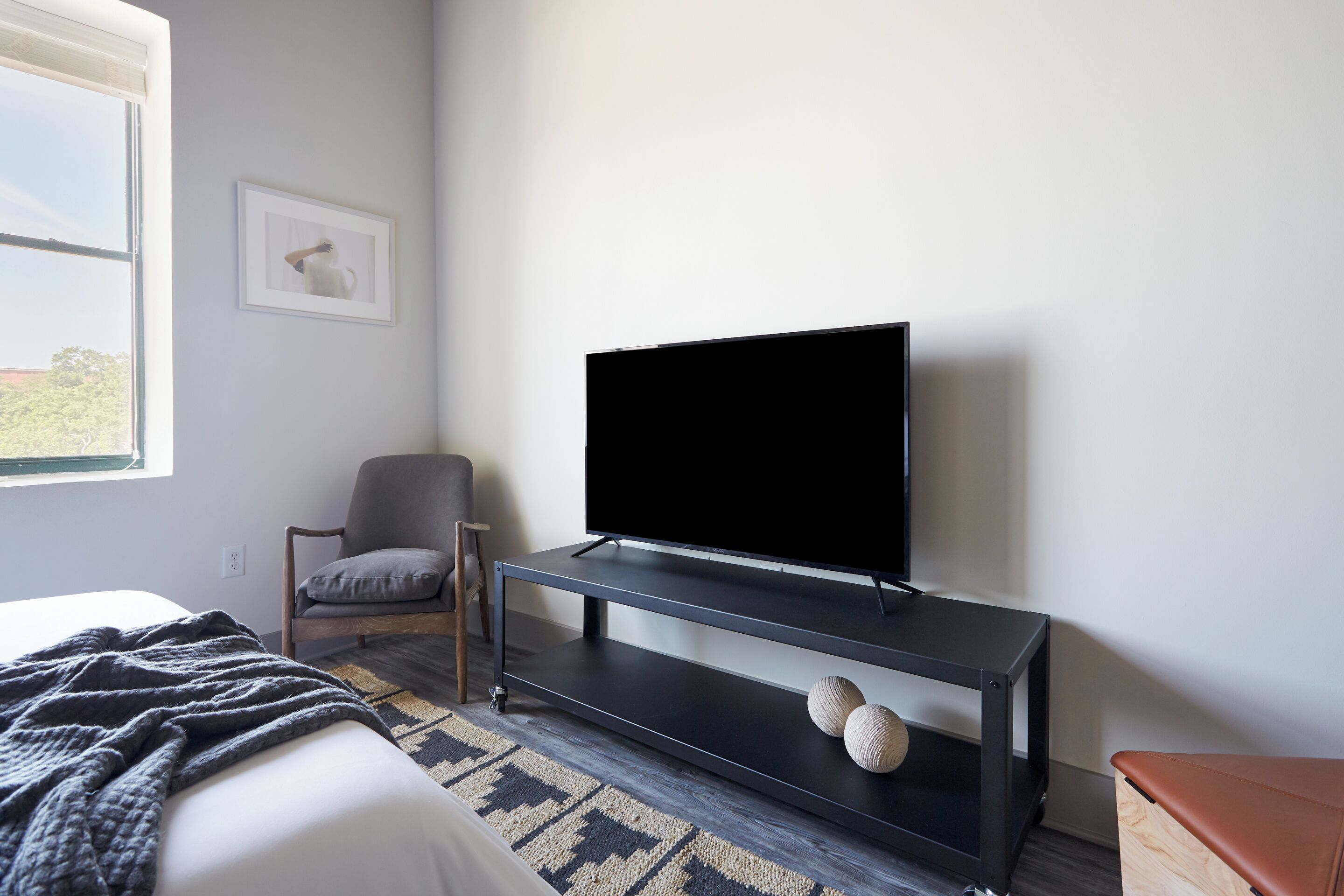 A modern bedroom with a bed, a TV on a black stand, a chair, and a window.