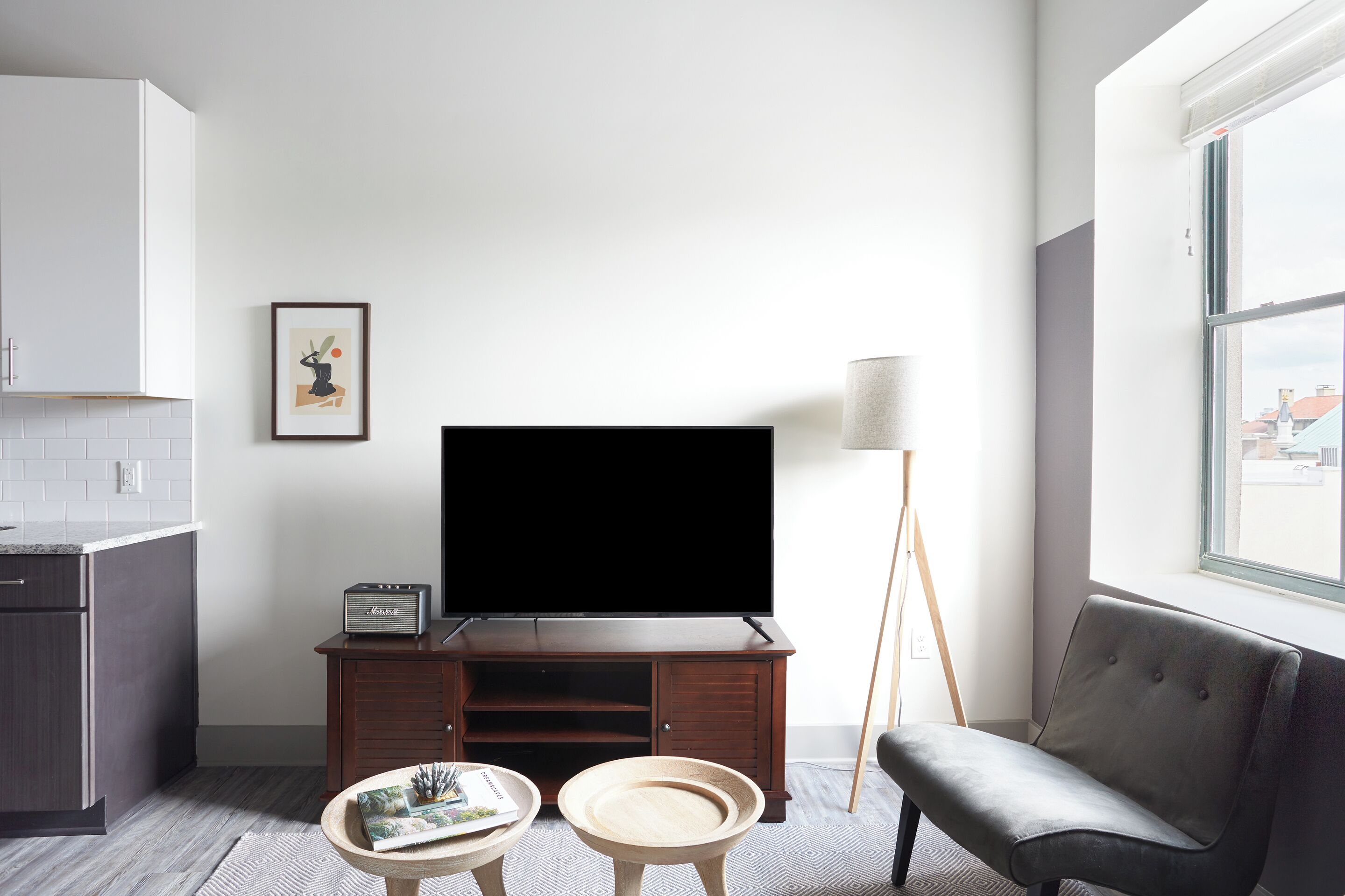 A modern living room with a flat-screen TV, a wooden cabinet, a round wooden table, and a grey sofa.