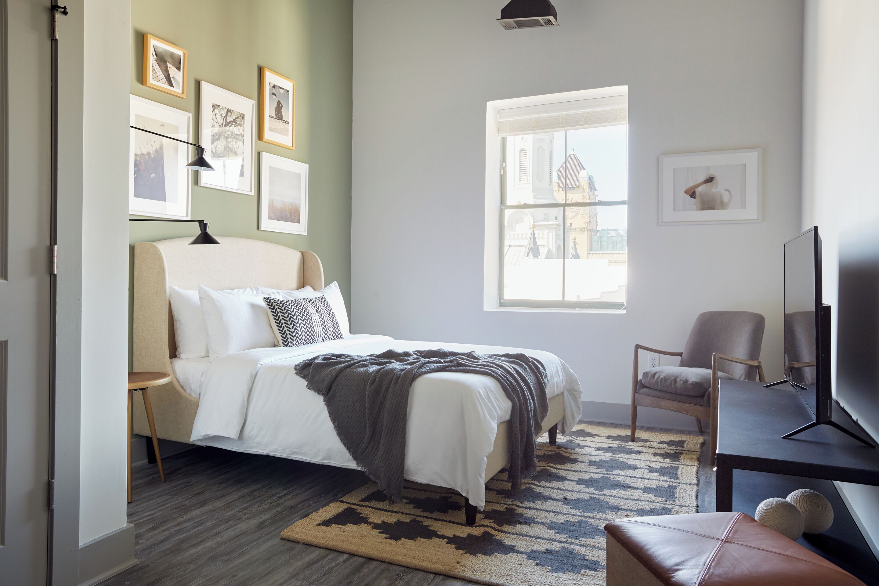 A bedroom with a bed, a chair, a TV, and a window.