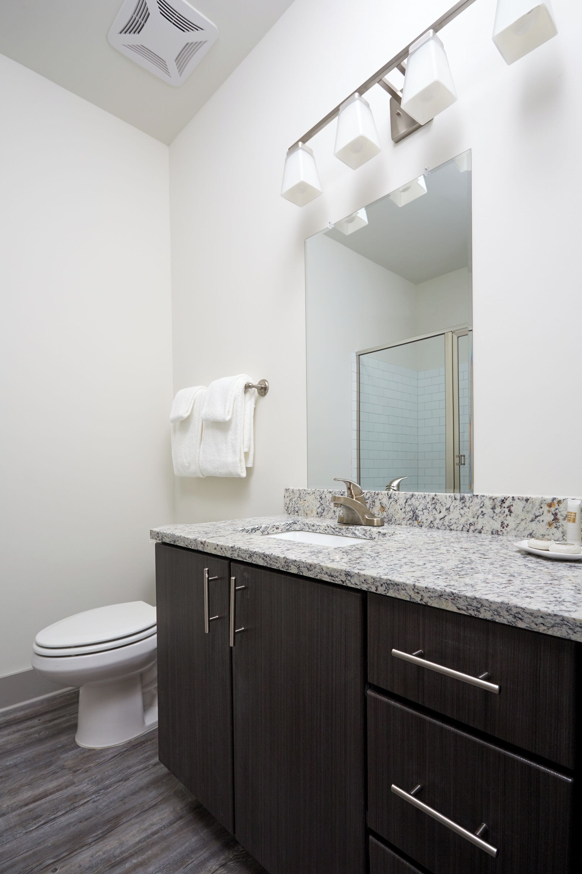 A modern bathroom with a white toilet, dark wooden cabinets, a marble countertop, and a large mirror with built-in lighting.