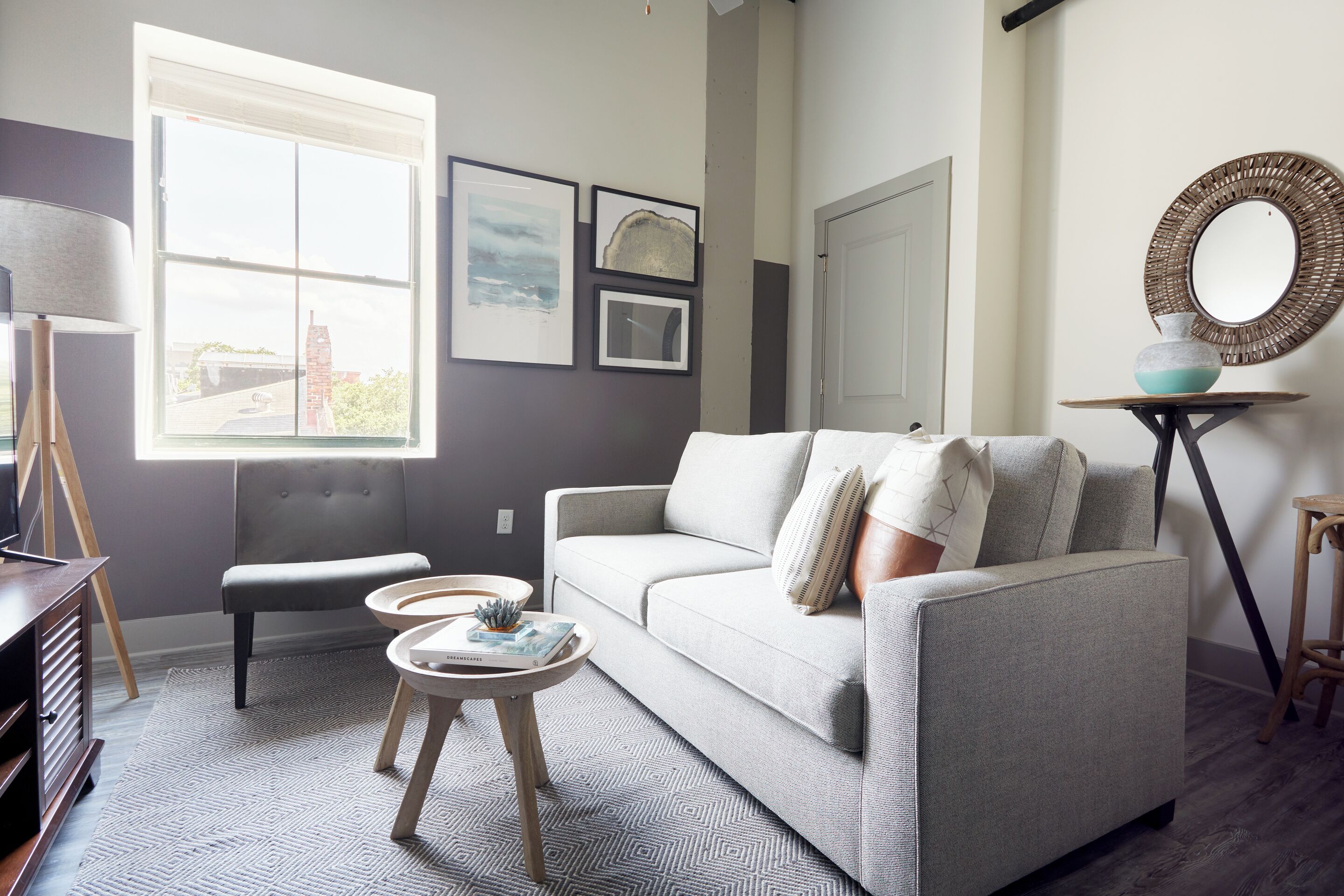 Una sala de estar moderna con un sofá gris, una mesita redonda y un ventanal amplio.