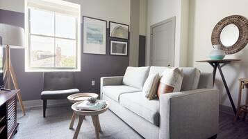 Una sala de estar moderna con un sofá gris, una mesita redonda y un ventanal amplio.