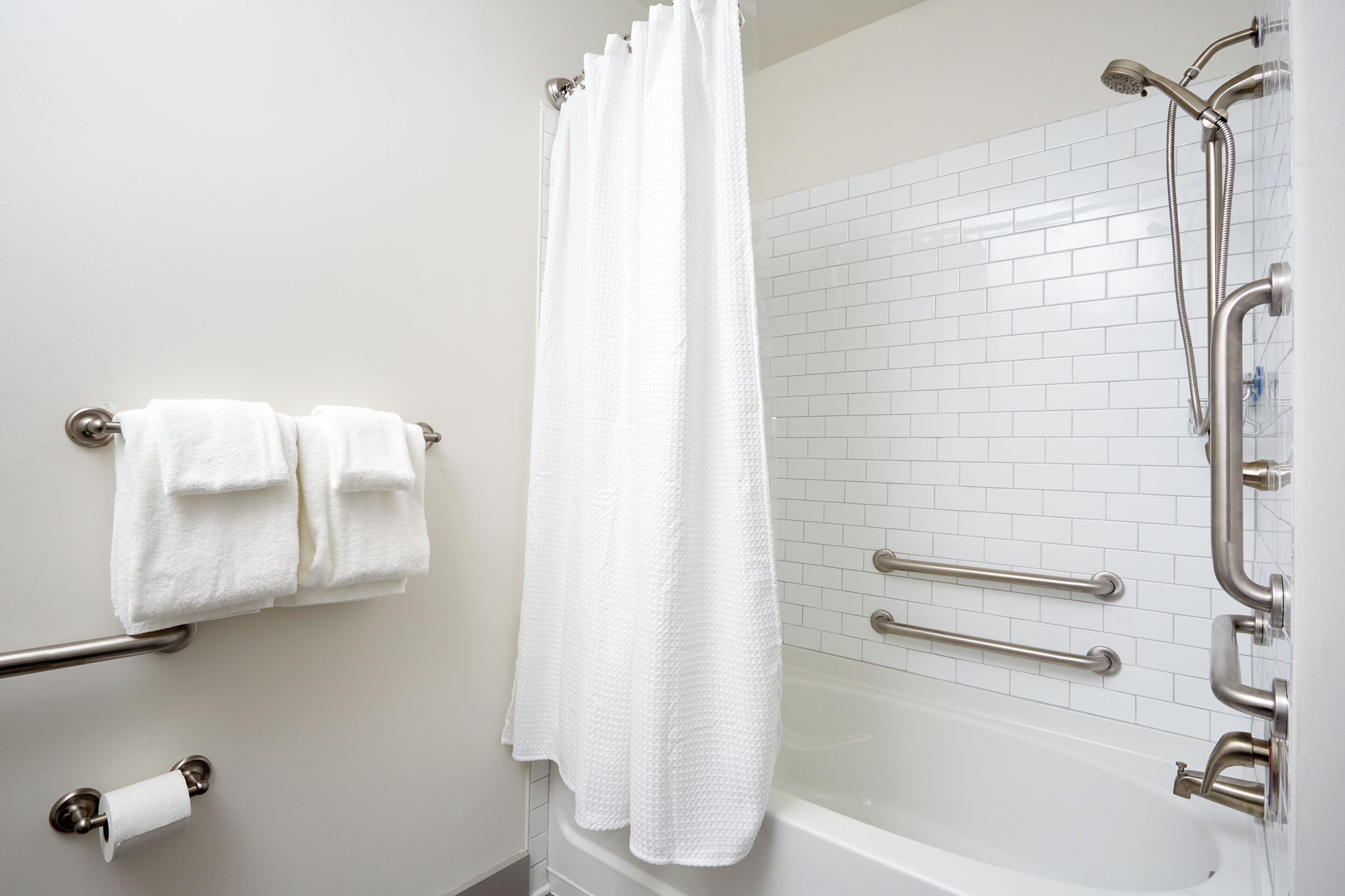 A modern bathroom with a white bathtub, a shower with a handheld showerhead, and a towel rack with two towels.