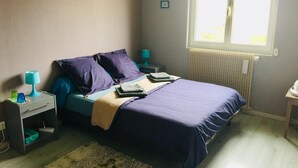 A bedroom with a bed, two bedside tables, a nightstand, a window, and a radiator. - Jolie halte normande (Balines)