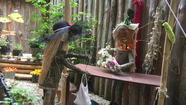 A rustic outdoor setting with a wooden fence, various plants, and a decorative figure. - Jolie halte normande (Balines)