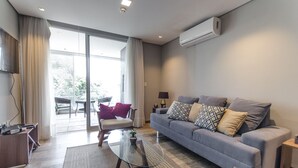 A modern living room with a grey sofa, a glass coffee table, and a view of the outdoors through large sliding doors. - OXO Bertoni Luxury in Villamorra (Asunción)