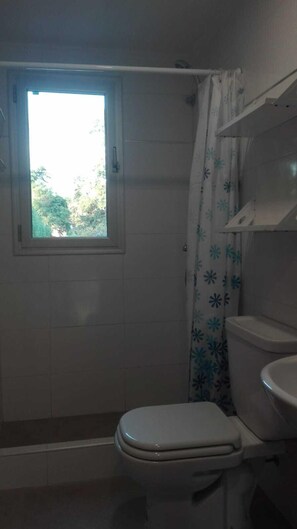 A bathroom with a toilet, a shower, and a window. - Alojamiento La Roja (Chascomus)