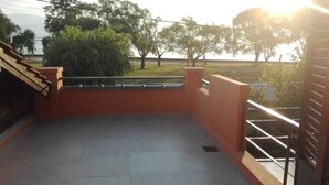 A rooftop terrace with a tiled floor, a metal railing, and a view of trees and a distant body of water. - Alojamiento La Roja (Chascomus)