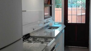 A kitchen with a gas stove, oven, and a sink. There is a window with a view of the outside. - Alojamiento La Roja (Chascomus)