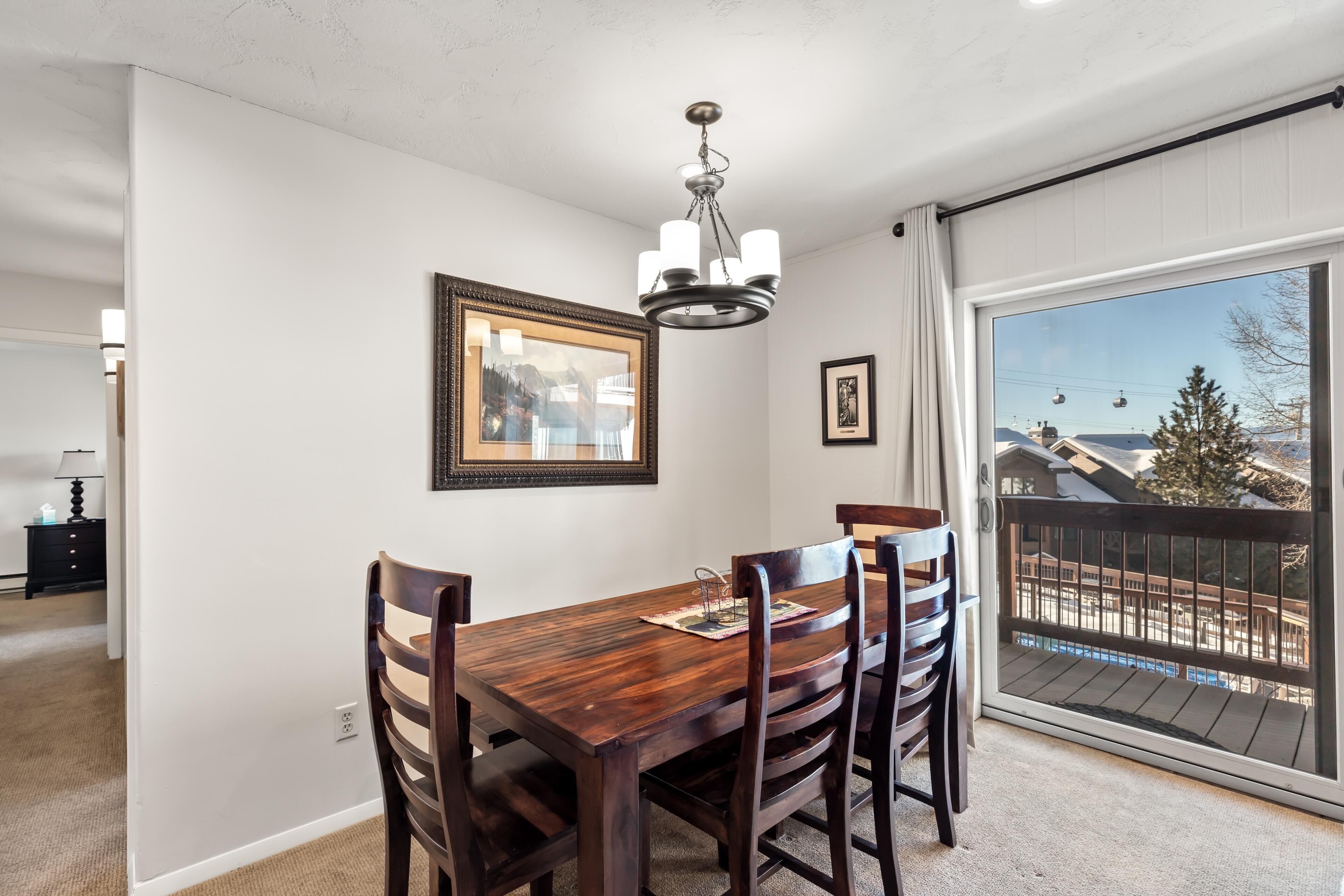 A dining area with a wooden table and chairs, a chandelier, and a large window with a view of a ski resort.