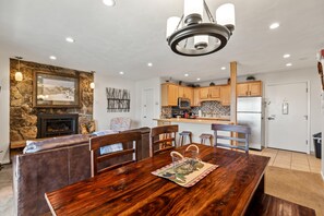 A dining area with a wooden table and chairs, a stone fireplace, and a kitchen with wooden cabinets and a refrigerator. - Lift Tickets Ski To Your Door, Wifi, Deck, Hot Tub (Steamboat Springs)