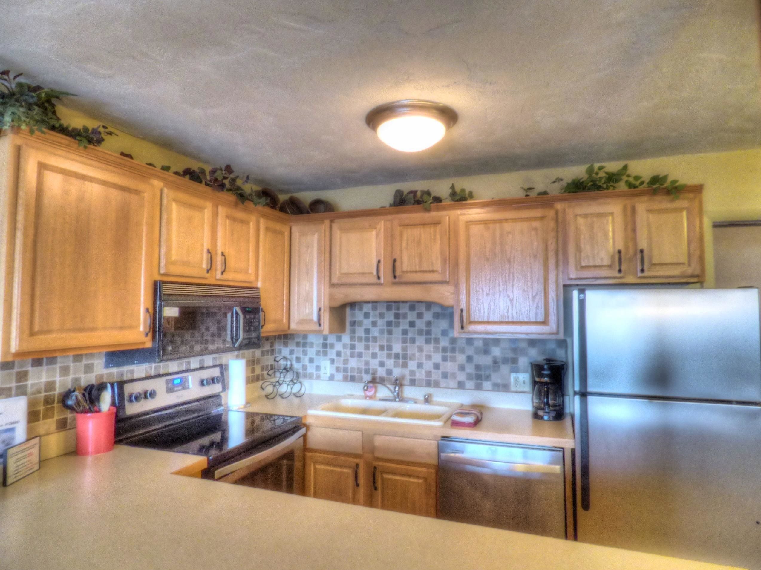 A kitchen with wooden cabinets, a stainless steel refrigerator, a microwave, an oven, and a sink.
