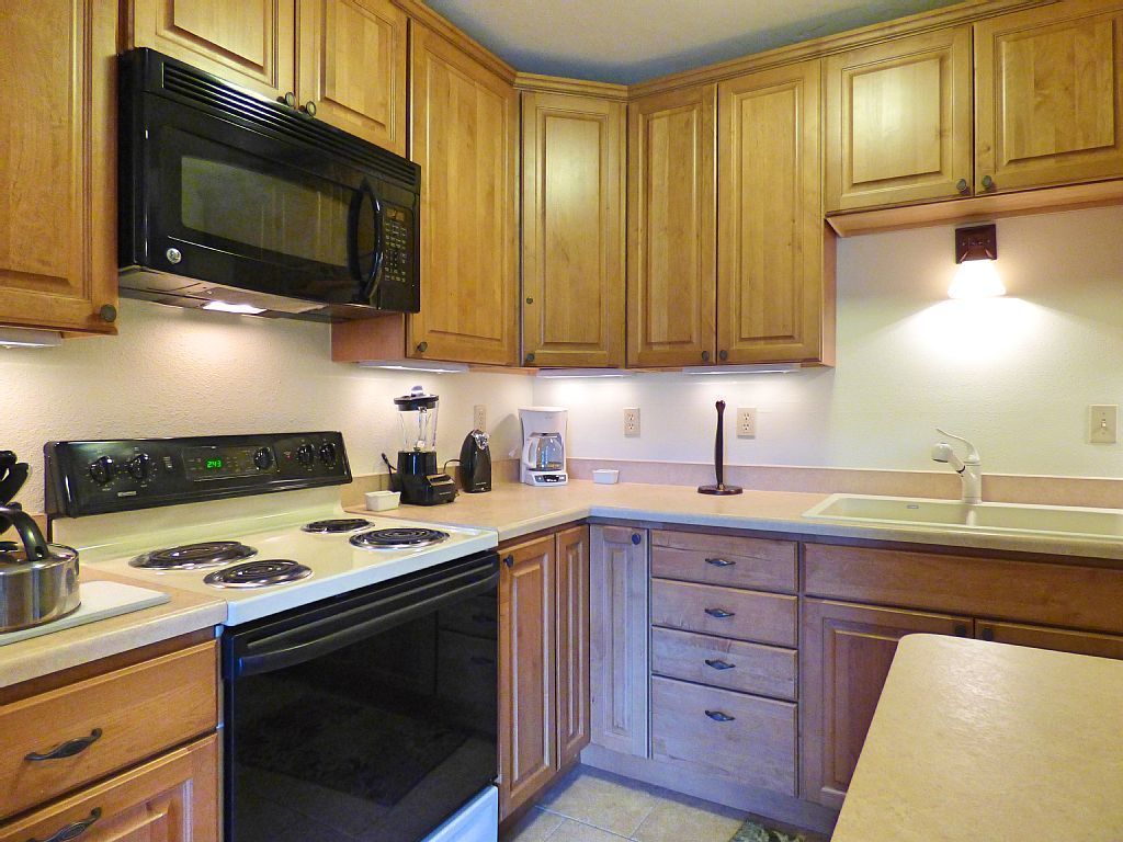 A kitchen with wooden cabinets, a black microwave, a stove, and a coffee maker.