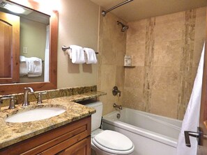 A bathroom with a granite countertop sink, a toilet, and a bathtub.
