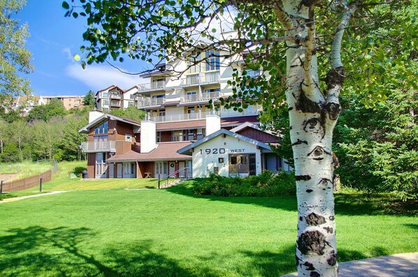 A multi-story residential building with a prominent '1920 WEST' sign, surrounded by lush greenery and a well-maintained lawn.