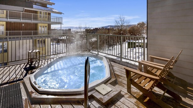 A hot tub on a wooden deck with a view of a snowy landscape and buildings in the background. - Mountain Village 2 Level Steps to Ski (Steamboat Springs)