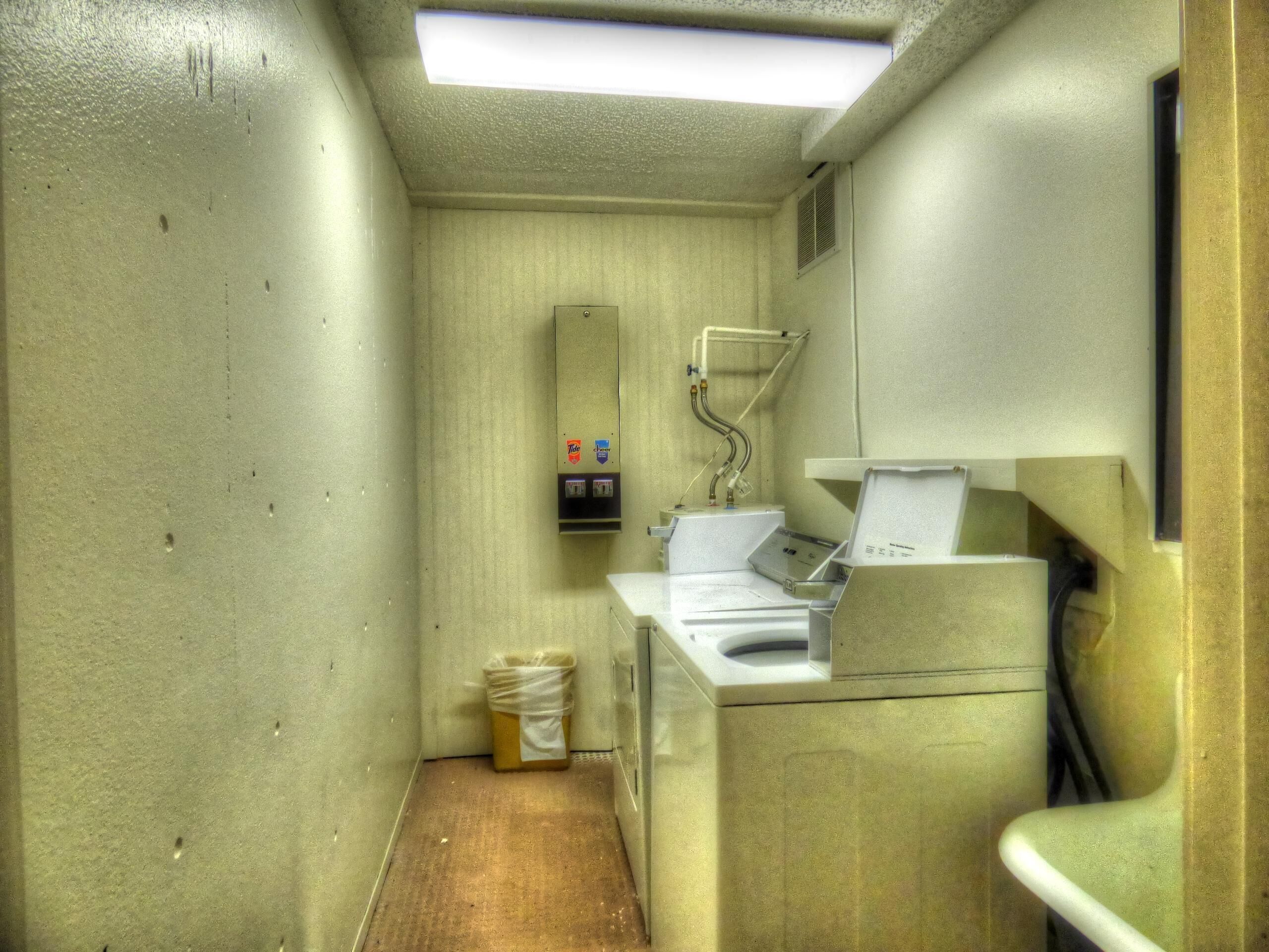 A compact, utilitarian bathroom with a single sink, a mirror, and a trash bin.
