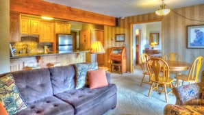 A cozy living room with a sofa, a dining table with chairs, a kitchen area with wooden cabinets and appliances, and a hallway leading to another room. - Lift Tickets Ski In Access & Hot Tub, Perfect For Couples (Steamboat Springs)