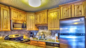 A kitchen with wooden cabinets, a stainless steel refrigerator, a microwave, and a granite countertop. - Lift Tickets Ski In Access & Hot Tub, Perfect For Couples (Steamboat Springs)