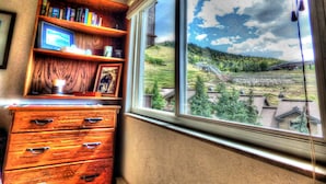 A room with a wooden dresser, a bookshelf, and a window with a view of a green landscape. - Lift Tickets Ski In Access & Hot Tub, Perfect For Couples (Steamboat Springs)