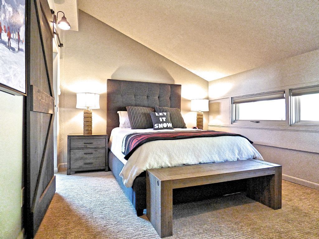 A bedroom with a large bed, two bedside lamps, a bench, and a window.