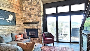 A cozy living room with a stone fireplace, a sofa with a 'Ski Lodge' pillow, and a red patterned rug. - Lift Tickets Perfect Penthouse Rustic Finishes Fireplace (Steamboat Springs)